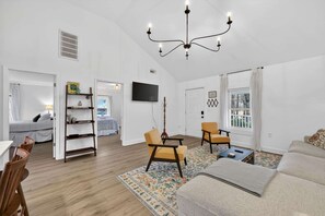A spacious living room with a chandelier, a television, a sofa, and a dining area with chairs. - Cozy 3BR Cottage Sauna Minutes to Davidson (Mooresville)