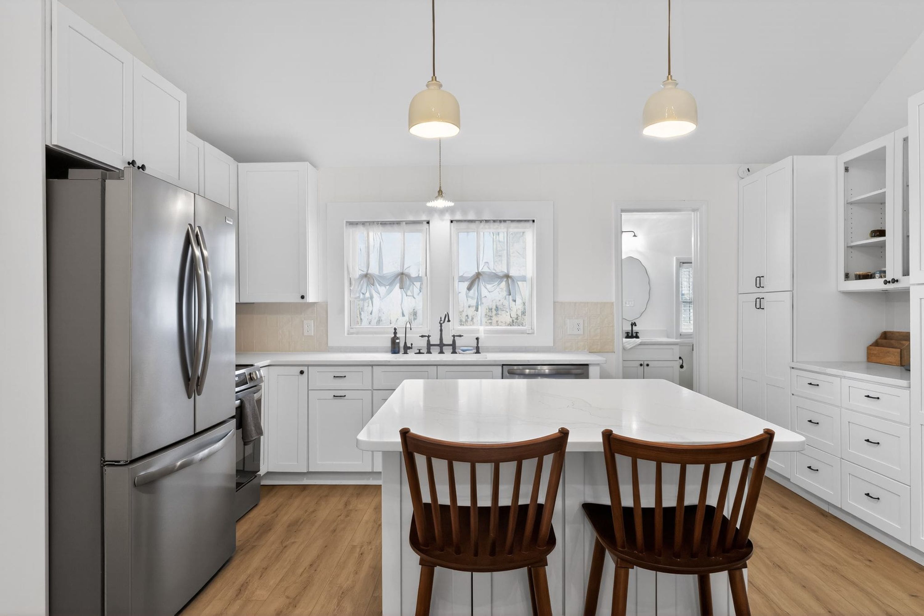 A modern kitchen with white cabinetry, stainless steel appliances, and a central island with two wooden chairs.