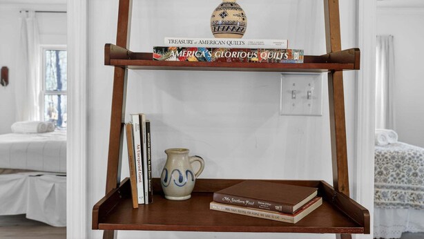 A shelf with a book titled 'Treasury of American Quilts' and a decorative vase. - Cozy 3BR Cottage Sauna Minutes to Davidson (Mooresville)