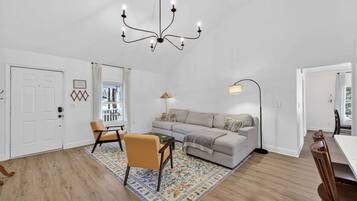 Una sala de estar moderna con un sofá, sillones, una mesa de centro, una araña y un comedor.