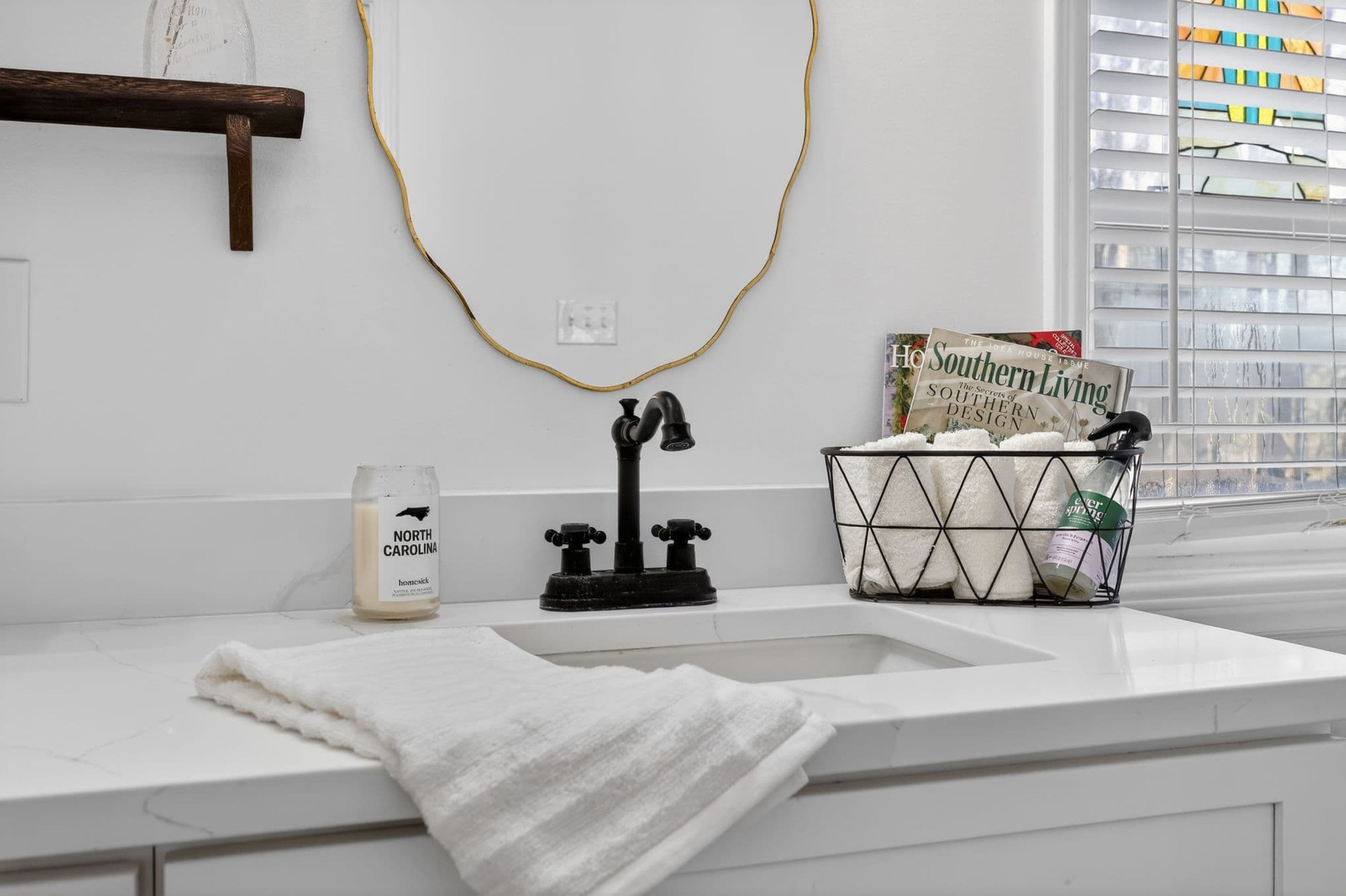 A bathroom with a white countertop, a black faucet, a bottle of North Carolina soap, a towel, and a magazine on the windowsill.