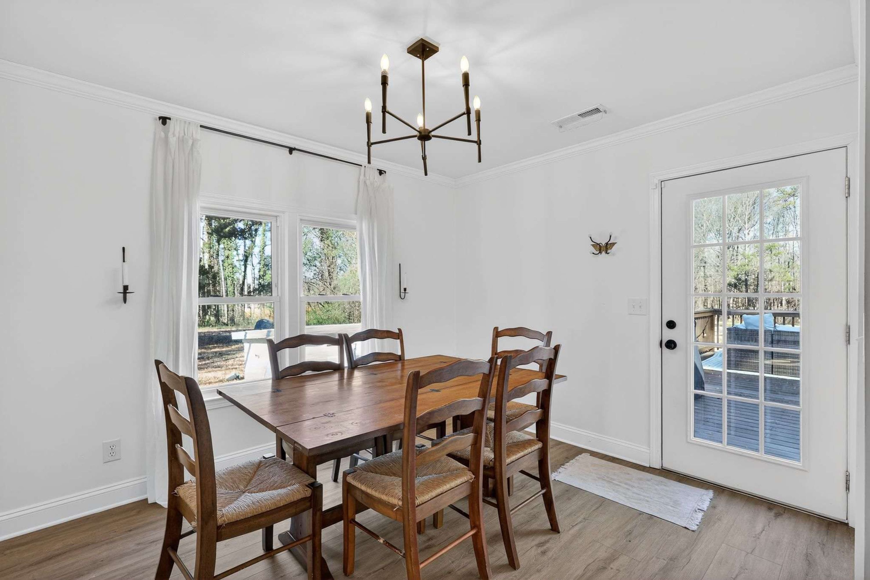 A dining room with a wooden table and chairs, a chandelier, and a door leading to an outdoor area.