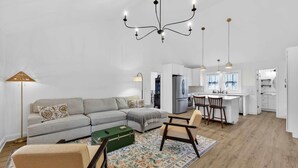 A modern living room with a sofa, a green trunk, and a patterned rug. - Cozy 3BR Cottage Sauna Minutes to Davidson (Mooresville)