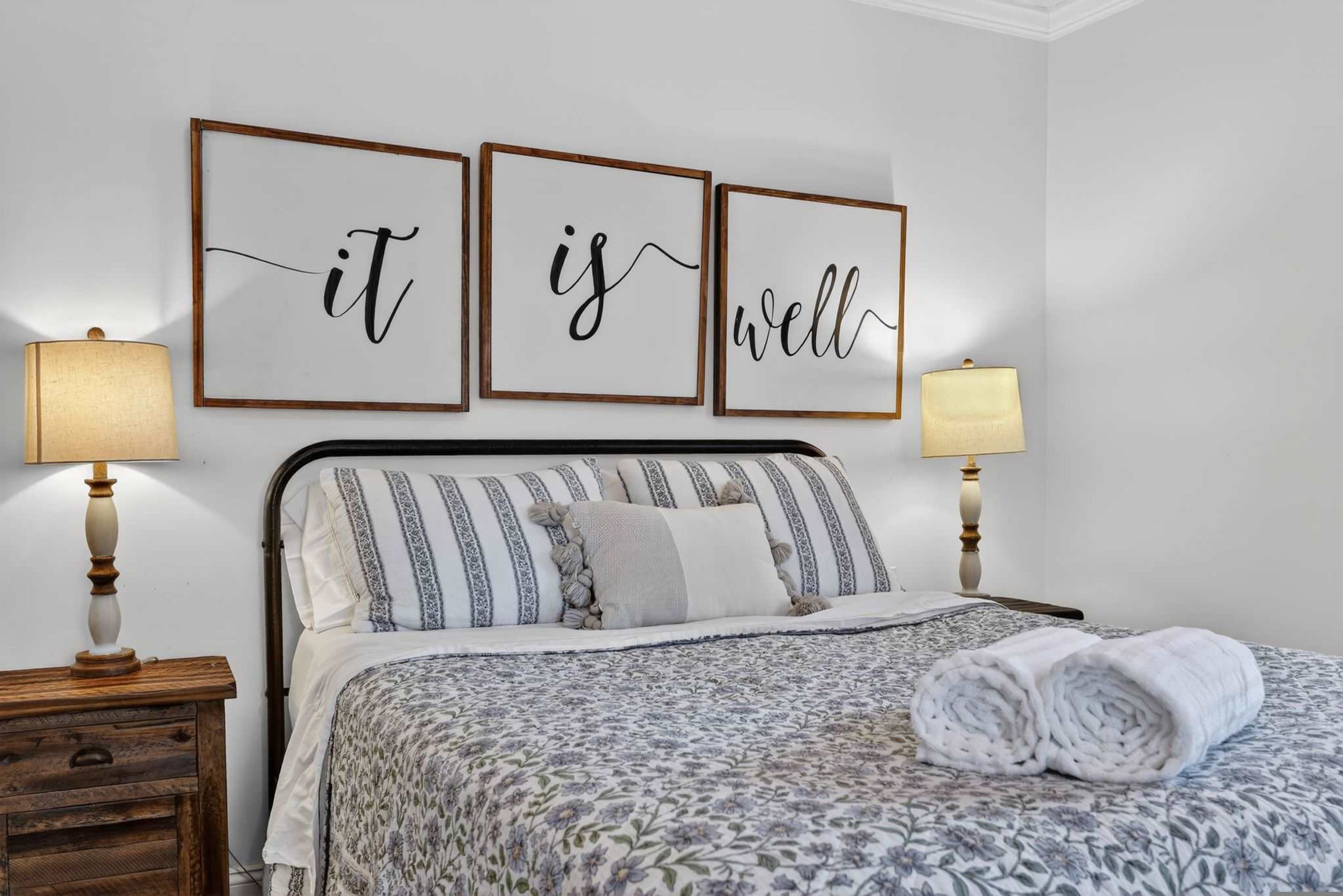A neatly made bed with striped bedding and a floral-patterned duvet, flanked by two bedside lamps and a wooden nightstand.