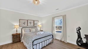 A bedroom with a bed, bedside lamps, a wooden nightstand, a window with curtains, and a desk with a chair. - Cozy 3BR Cottage Sauna Minutes to Davidson (Mooresville)