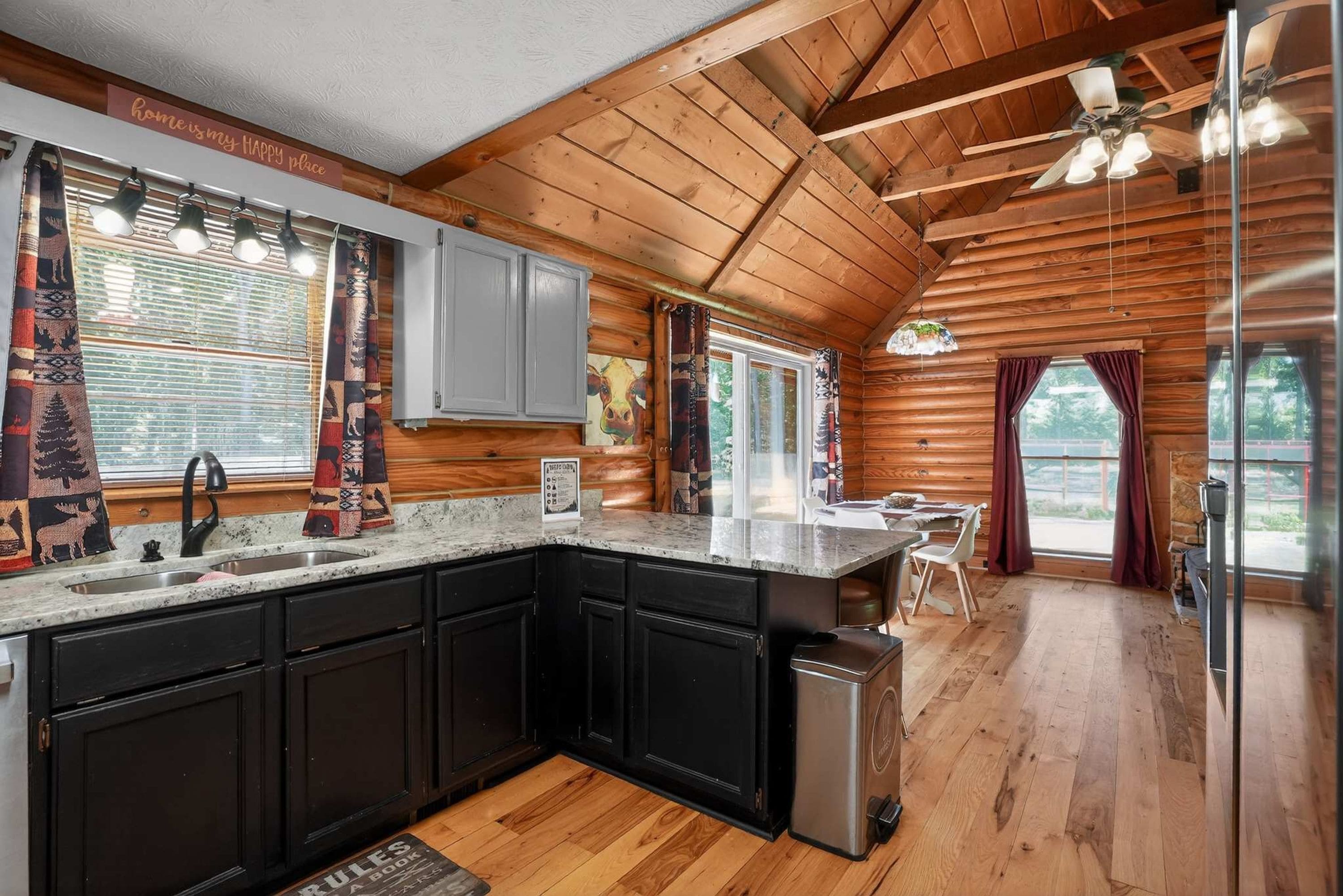 A log cabin interior with a kitchen, dining area, and a view of the outdoors.
