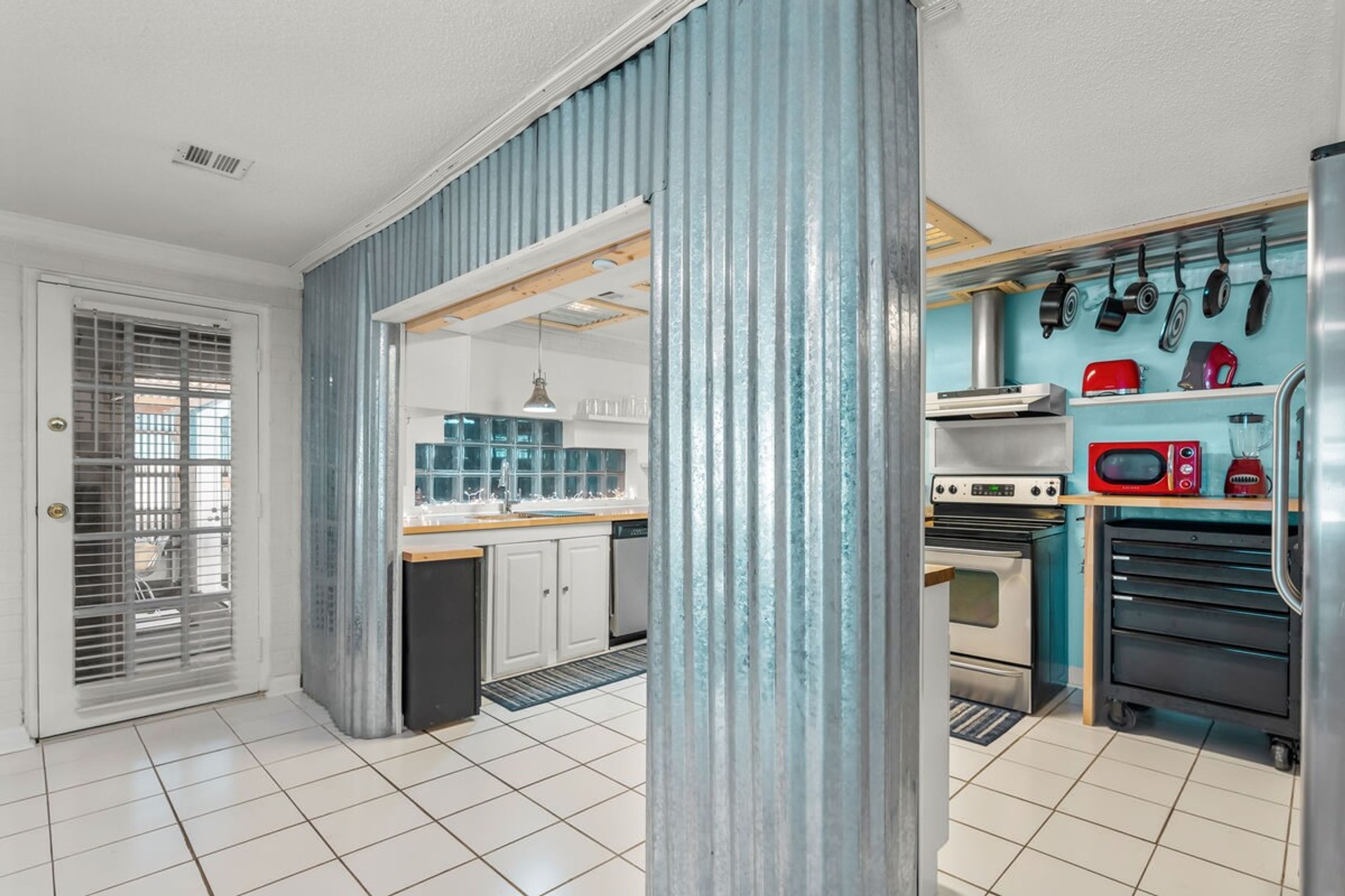 A compact kitchen with a built-in oven, microwave, and a variety of cookware hanging on the wall.