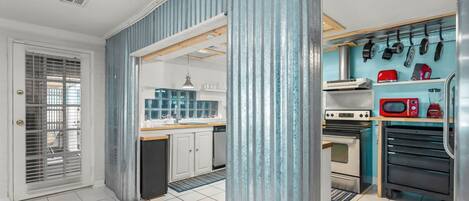 A compact kitchen with a built-in oven, microwave, and a variety of cookware hanging on the wall.