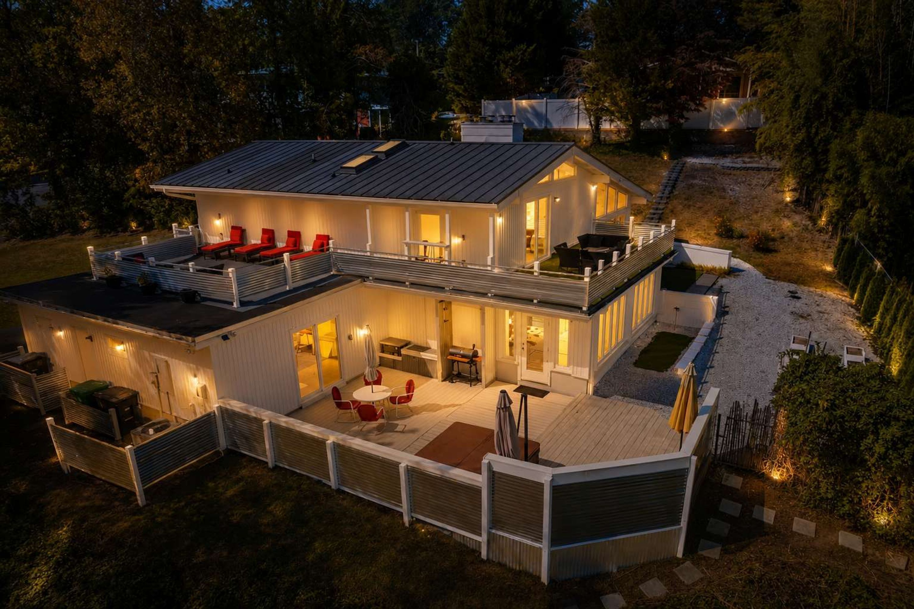 A modern two-story house with a covered patio, outdoor seating, and a well-lit interior.