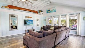 A living room with a large sectional sofa, wooden flooring, a ceiling fan, and a sailboat decoration. - Beach Life 3 - Sunshine Lane (Treasure Island)