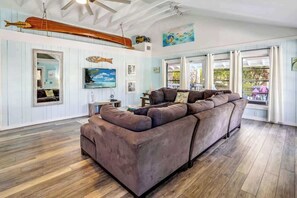 Ein Wohnzimmer mit einem großen Ecksofa, Holzböden, einem Deckenventilator und einer Segelschiff-Dekoration.