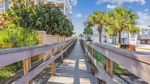 A wooden boardwalk leading to a building with balconies, surrounded by greenery and palm trees. - Beach Life 3 - Sunshine Lane (Treasure Island)