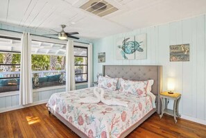 Una camera da letto con un letto, una ventola a soffitto, una finestra con tende e un quadro di una tartaruga oltre a un cartello.