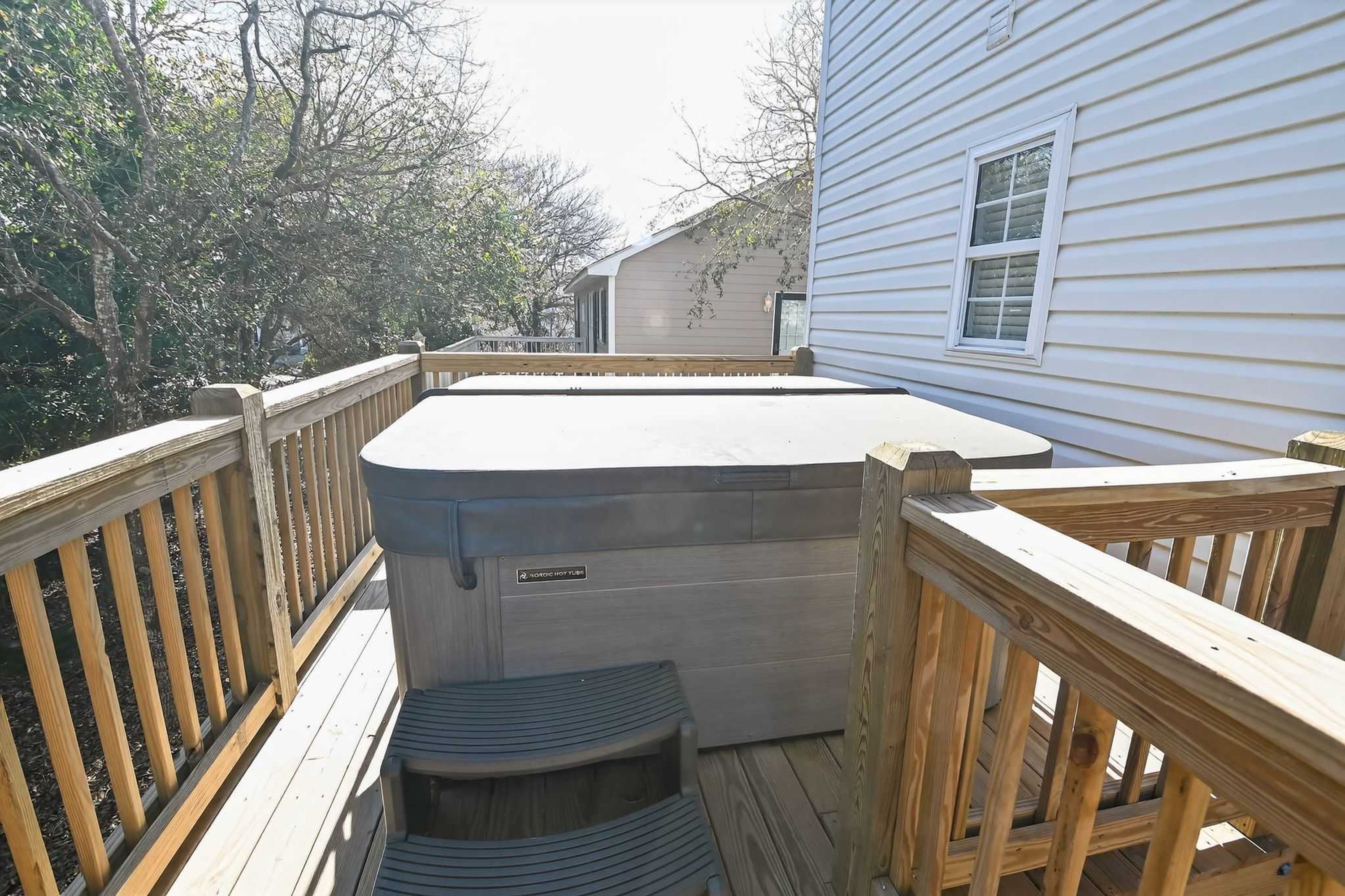 A hot tub on a wooden deck with a house in the background.