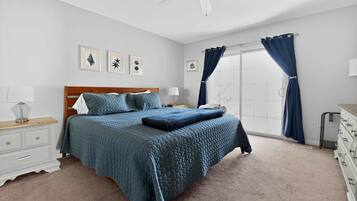 A bedroom with a bed, nightstands, a dresser, a ceiling fan, and a window with curtains.