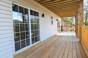 A covered porch with a wooden deck, large sliding glass doors, and a small window. - Coastal 4BR Retreat Hot tub Water Views Deck Pet-friendly (Holly Ridge)