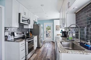 A modern kitchen with white cabinets, a stainless steel refrigerator, a microwave, and a sink with a faucet. - The Gulf House | Walk to Beach | 5BR Retreat (Treasure Island)