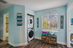 A laundry room with a washing machine, a drying rack, and a wall with nautical-themed decor. - The Gulf House | Walk to Beach | 5BR Retreat (Treasure Island)