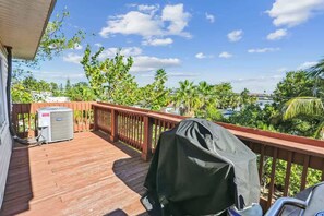 A wooden deck with a barbecue grill, an air conditioning unit, and a covered grill on a sunny day. - The Gulf House | Walk to Beach | 5BR Retreat (Treasure Island)