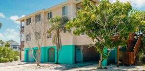 A multi-story building with a flat roof, a garage, and a small tree in the foreground. - The Gulf House | Walk to Beach | 5BR Retreat (Treasure Island)