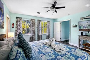 Ein Schlafzimmer mit Bett, Vorhängen, Deckenventilator, Tür und Fernseher.
