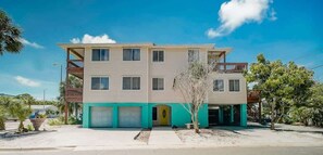 A multi-story residential building with a flat roof, a balcony on the second floor, and a small tree in front. - The Gulf House | Walk to Beach | 5BR Retreat (Treasure Island)