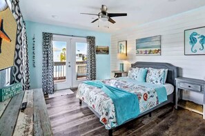A bedroom with a bed, a nightstand, a ceiling fan, and a view of the outdoors. - The Gulf House | Walk to Beach | 5BR Retreat (Treasure Island)