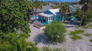 A turquoise house with a deck and outdoor seating, surrounded by palm trees and greenery. - Beach Life 2 - Sunshine Lane (Treasure Island)