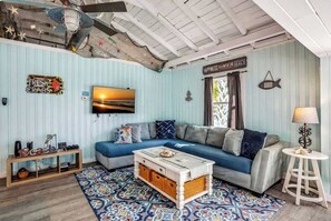 Ein Zimmer mit blauen Streifen an der Wand, einem Sofa, einem Couchtisch, einem Fernseher und einem Deckenventilator.