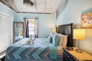 A hotel room with a bed, a nightstand, a lamp, and a window with curtains. - Beach Life 2 - Sunshine Lane (Treasure Island)
