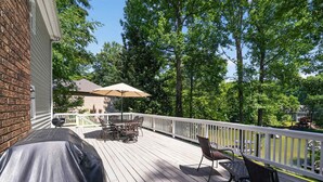 Eine Holzterrasse mit Gartenmöbeln, einem Grill und Blick auf einen See.