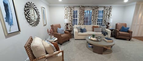 A living room with a beige sofa, two armchairs, a coffee table, and a decorative wall piece.