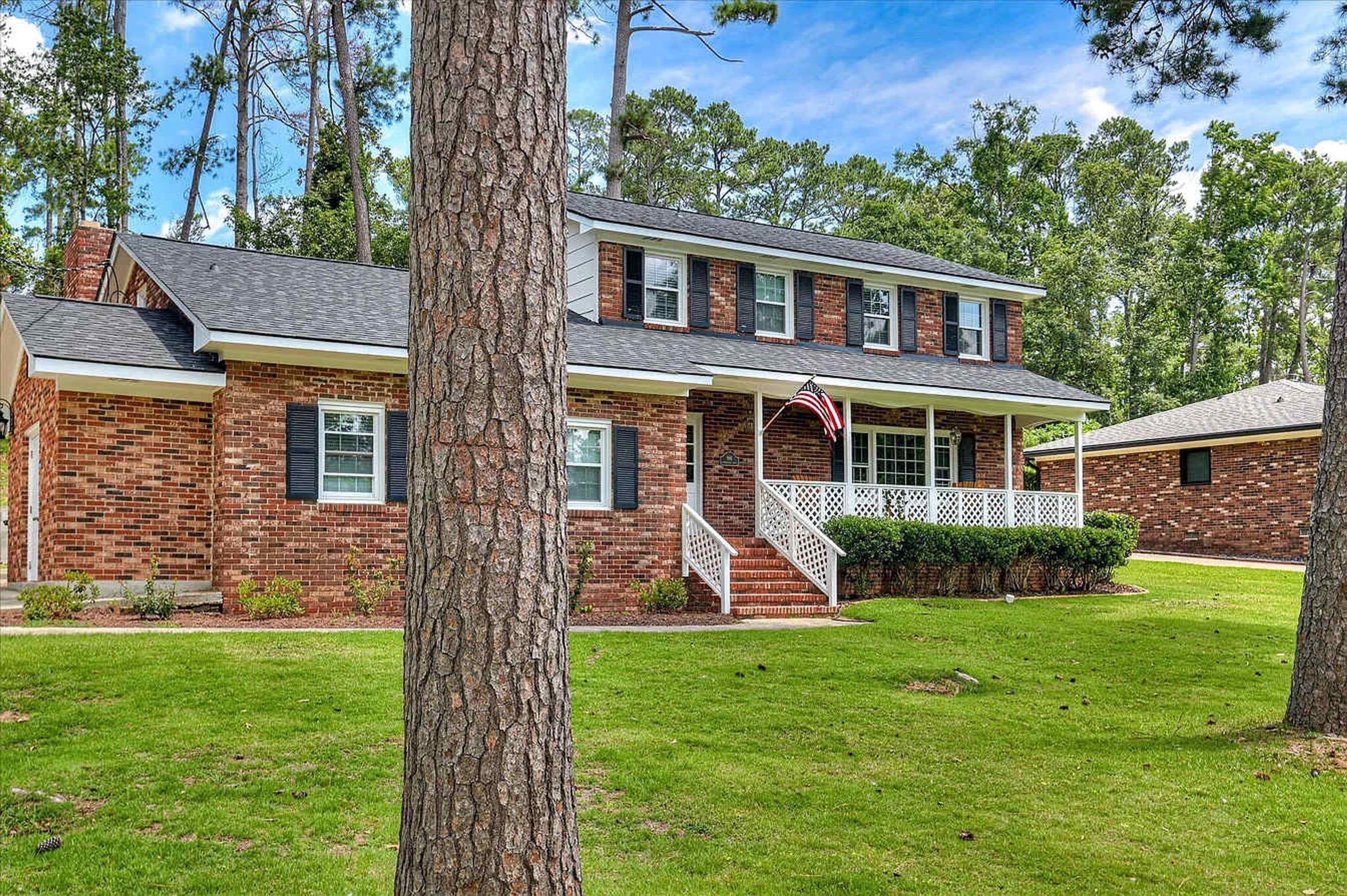 A two-story brick house with a front porch, a small deck, and a flag.