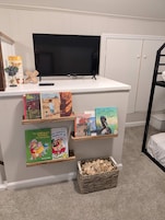 Una estantería infantil con varios libros y un televisor encima.