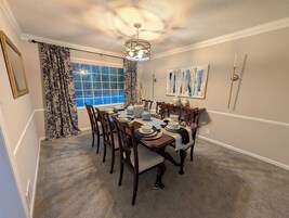 Comedor con una mesa grande dispuesta para seis personas, rodeado de sillas de madera.