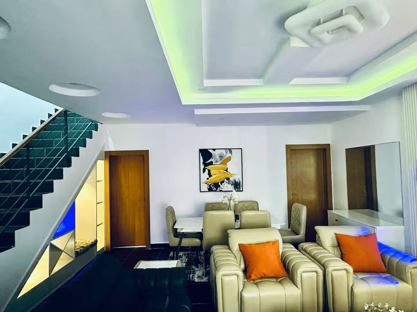 A modern living room with a sofa set, a dining table, and a staircase.
