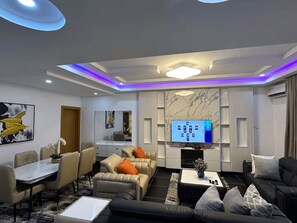 A modern living room with a flat-screen TV, leather sofas, a dining area, and a marble wall. - Luxury 5-Bedroom Apartment in Lekki 1 with Snooker, Fast Wi-Fi & 24/7 Power (Lagos)