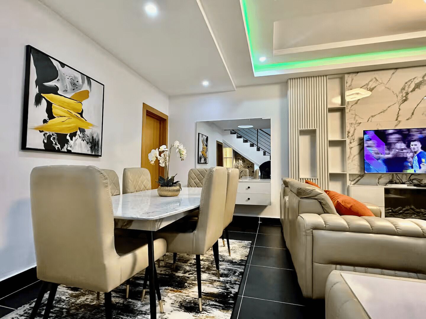Een moderne woonkamer met een eethoek, een bank, een televisie en kunstwerken aan de wanden.