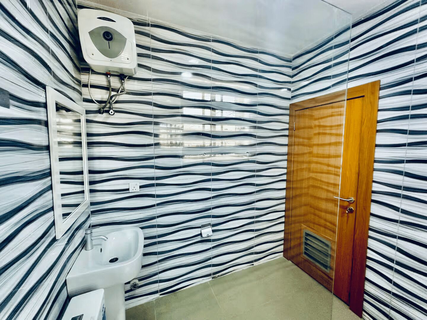 A bathroom with a patterned wall, a wooden door, and a white sink.