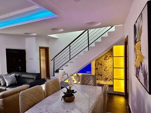 A modern living room with a staircase, a dining area, and a sofa. - Luxury 5-Bedroom Apartment in Lekki 1 with Snooker, Fast Wi-Fi & 24/7 Power (Lagos)