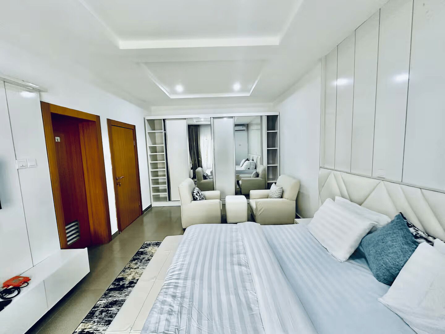 Een moderne slaapkamer met een groot bed, een zithoek met stoelen, een kledingkast en een inloopkast met schuifdeuren.