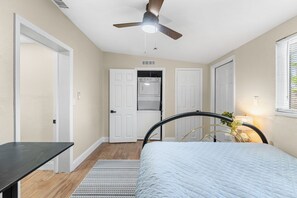 Une chambre avec un lit, un ventilateur de plafond, une fenêtre avec des stores, une porte, ainsi qu’un lave-linge et un sèche-linge encastrés.