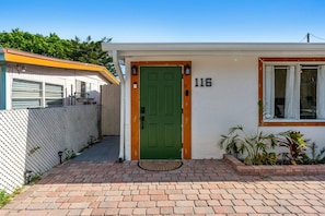 A single-story house with a green door, a number '116' on the wall, and a small window with curtains. - 116 Lincoln Ave (Cape Canaveral)
