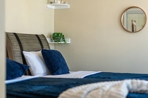 Ein Schlafzimmer mit einem Bett, Kissen, einer Zimmerpflanze, einem Spiegel und einem Regal mit Dekoration.