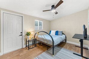 A bedroom with a bed, bedside table, lamp, ceiling fan, window, and a desk with a computer. - 116 Lincoln Ave (Cape Canaveral)