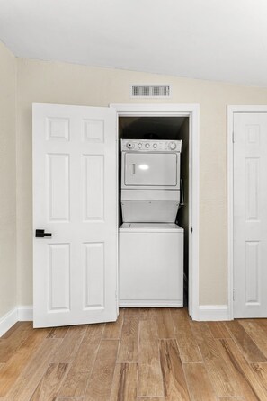 A compact laundry room with a stacked washer and dryer, a vent above the dryer, and a wooden floor. - 116 Lincoln Ave (Cape Canaveral)