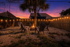 A backyard with a fire pit, outdoor seating, a palm tree, and a wooden fence. - 116 Lincoln Ave (Cape Canaveral)