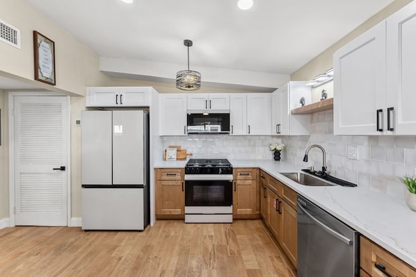 A modern kitchen with white cabinetry, a stainless steel refrigerator, a built-in oven, and a dishwasher. - 116 Lincoln Ave (Cape Canaveral)