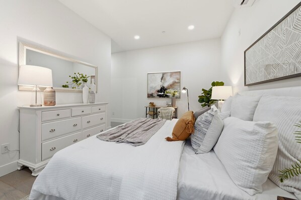 Un dormitorio con cama, cómoda, lámparas de noche y una obra de arte colgada en la pared.