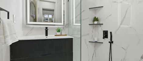A modern bathroom with a marble shower, a dark wood vanity, and a large mirror.